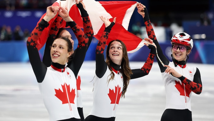 Elles brandissent le drapeau du Canada et sourient en regardant dans la foule.