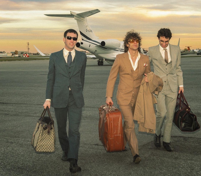 Trois hommes, valises à la main, marchent sur le tarmac d'un aéroport.