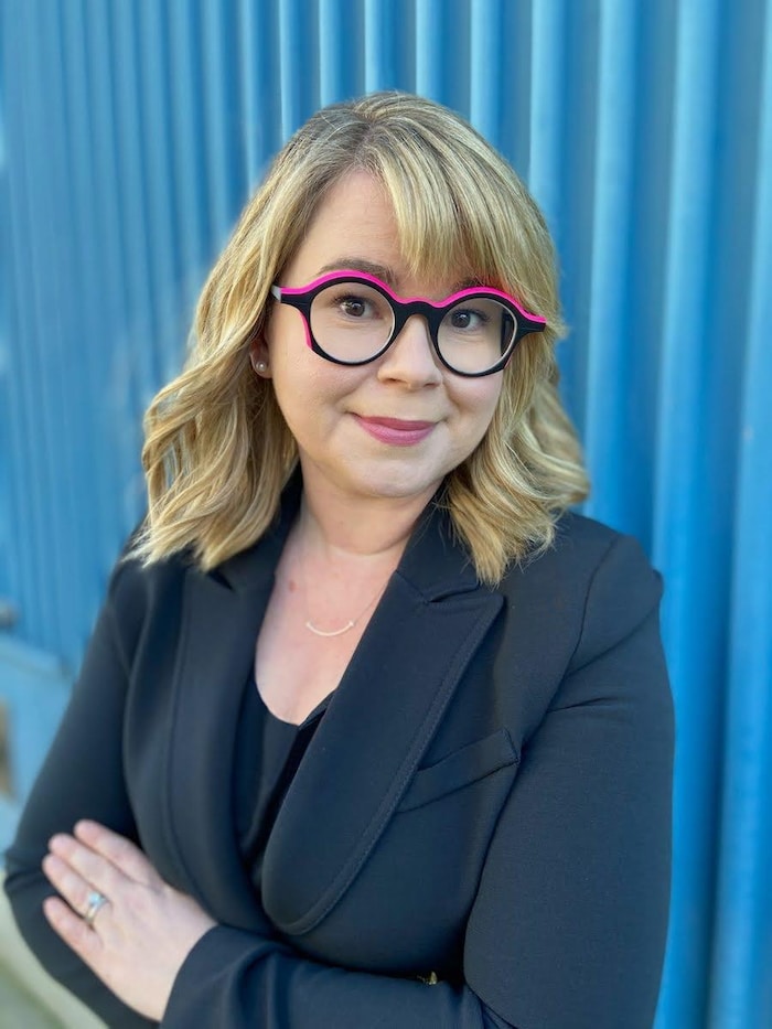 Une femme esquisse un sourire derrière des lunettes colorées.