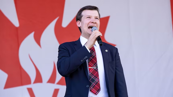 Le maire de Calgary, Jeromy Farkas, tient un microphone dans une main.