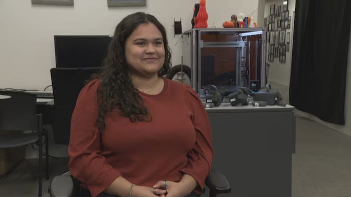 Une femme fixe du regard l'objectif d'une caméra dans un bureau.