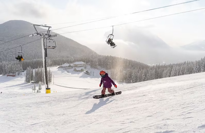 Un surfeur des neiges évolue le long d'une piste à côté d'une remontée mécanique.