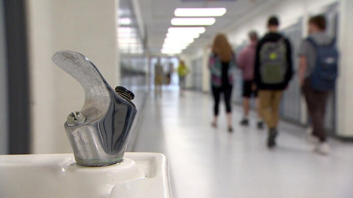 Un abreuvoir en premier plan et des élèves qui marchent au loin dans un corridor.