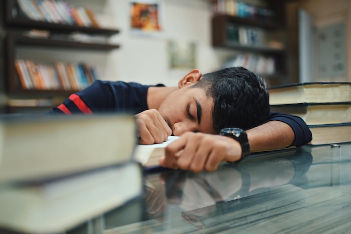 Un adolescent dort à la bibliothèque.