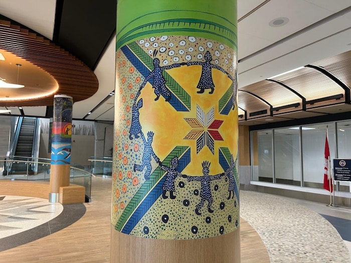 Des colonnes dans l'aéroport sont peintes. Celle à l'avant représente des personnes dansant en rond autour d'une lueur jaune et d'une étoile mi'kmaw à huit pointes.