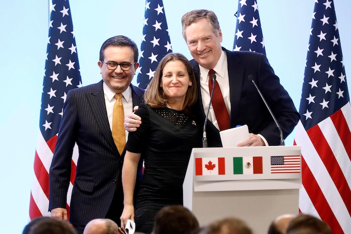 Deux hommes et une femme derrière une tribune, avec les drapeaux canadien, mexicain et américain. 