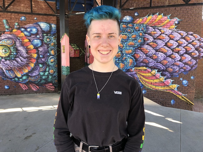 Alex Brownstein pose pour une photo debout sur une place publique devant une murale peinte qui représente un poisson multicolore.