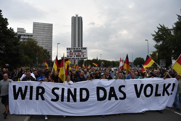 Des Allemands brandissent une longue banderole blanche sur laquelle il est écrit en lettres majuscules: « Nous sommes le peuple » en plus de brandir des drapeaux de l'Allemagne.