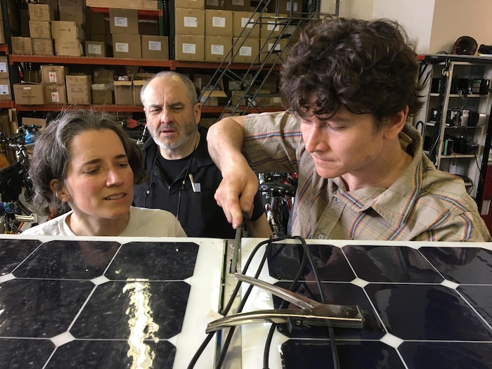 Un homme répare un panneau solaire, alors qu'une femme et un homme l'observent.