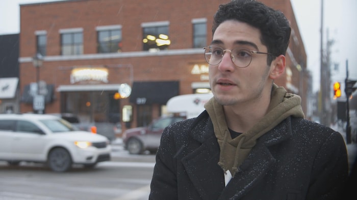 Un jeune homme à l'extérieur durant l'hiver. Il porte un manteau et semble regarder un intervieweur à la gauche de la caméra.