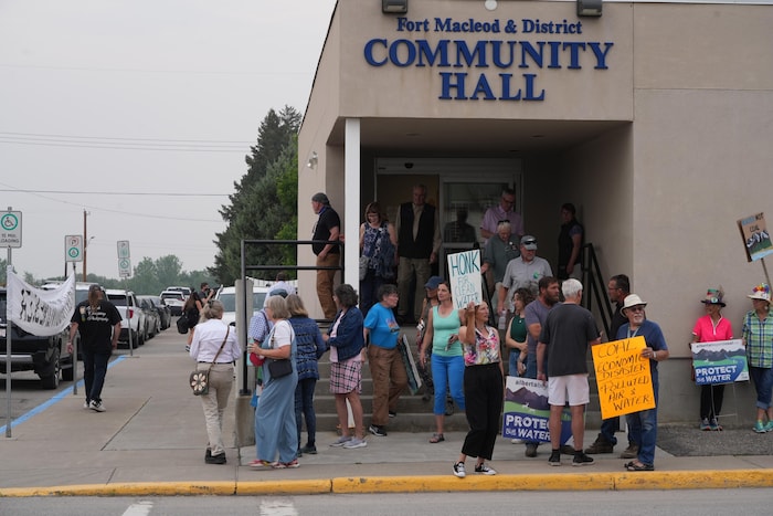 Des personnes portant des pancartes se tiennent devant un centre communautaire à Fort MacLeod, à l'occasion d'une rencontre publique sur l'exploitation minière en Alberta, le 11&nbsp;juin 2025.
