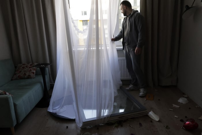 L'intérieur d'un appartement endommagé avec un homme qui regarde par la fenêtre. 