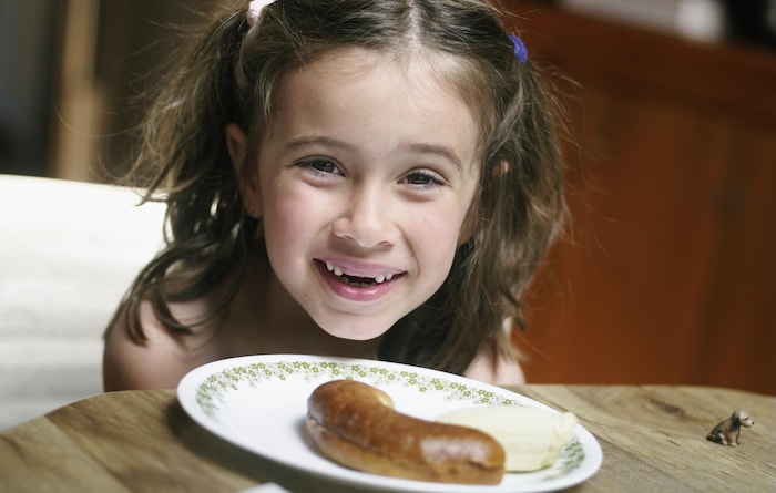 Une fillette sourit au-dessus d'une assiette contenant une moitié de bagel et un morceau de banane.