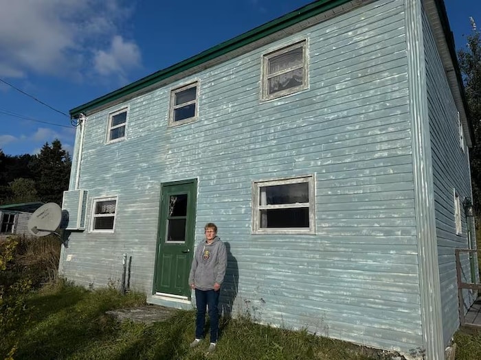 Elizabeth Power debout devant une maison à deux étages.