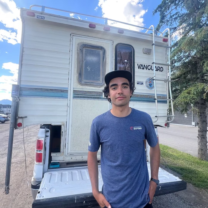 Un homme portant une casquette se tient devant une fourgonnette.