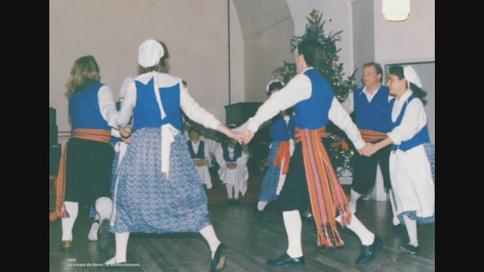Des danseurs habillés en habit traditionnel canadien-français qui se tiennent main dans la main. 