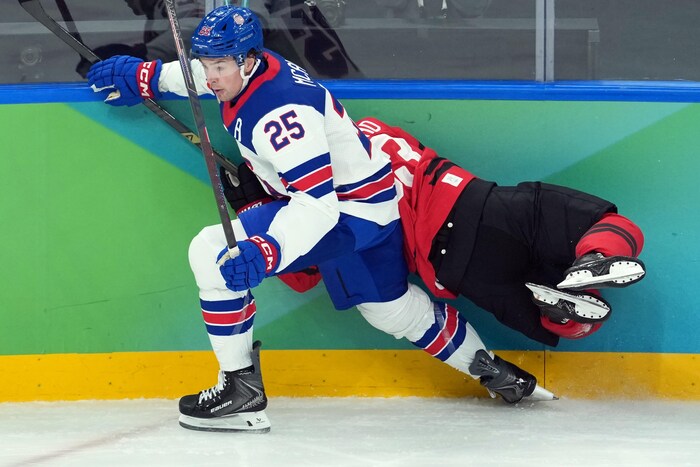Brad Marchand est écrasé contre la bande par un autre joueur. Il est photographié à l'horizontale, les genoux fléchis et ne touchant plus à la patinoire.