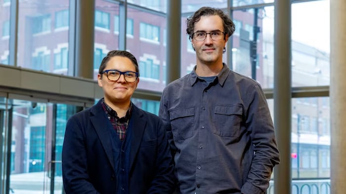 Deux personnes se tenant côte à côte fixent du regard l'objectif d'une caméra.