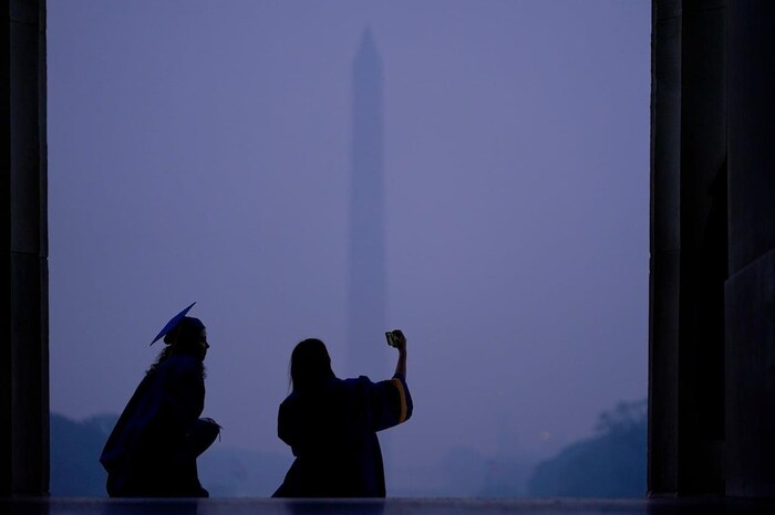 Two students celebrating their graduation from Robinson Secondary School in Fairfax, Va., pose for a selfie at the steps of the Lincoln Memorial as a thick layer of smoke and the Washington Memorial give backdrop to them on Thursday, June 8, 2023.