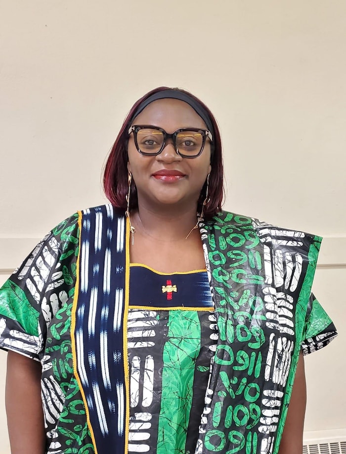 Une femme habillée en tenue traditionnelle camerounaise regarde devant elle.