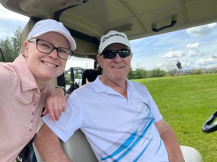 Une femme souriante se tient debout derrière un homme souriant, sur un parcours de golf.