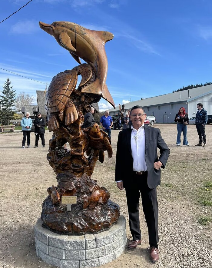 Le maire de Chetwyn, Allen Courtoreille, pose près d'une statue représentant notamment une tortue et un dauphin à Fraser Lake, en Colombie-Britannique, en mai 2025.