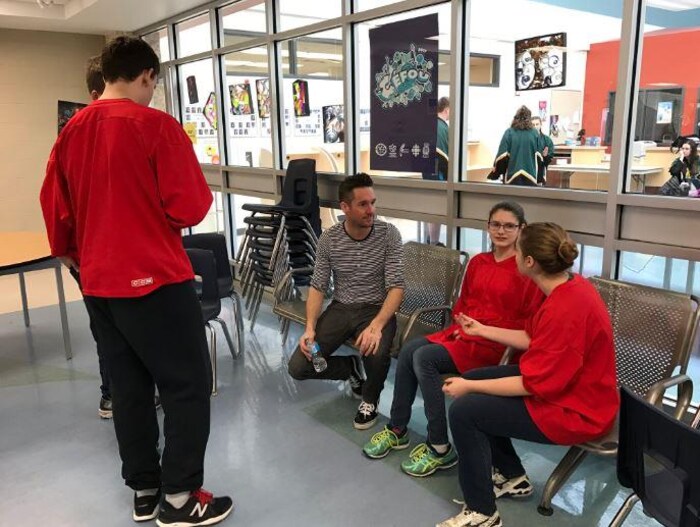 Quatre jeunes vêtus d'un chandail rouge discutent avec leur entraîneur d'improvisation dans une salle de classe.