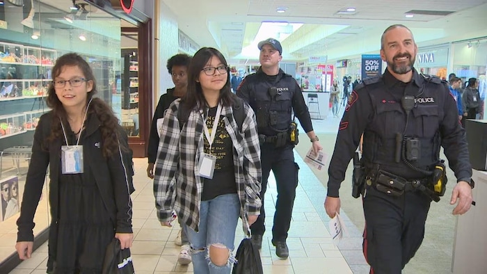 Deux policiers se promènent dans un centre commercial avec trois jeunes.