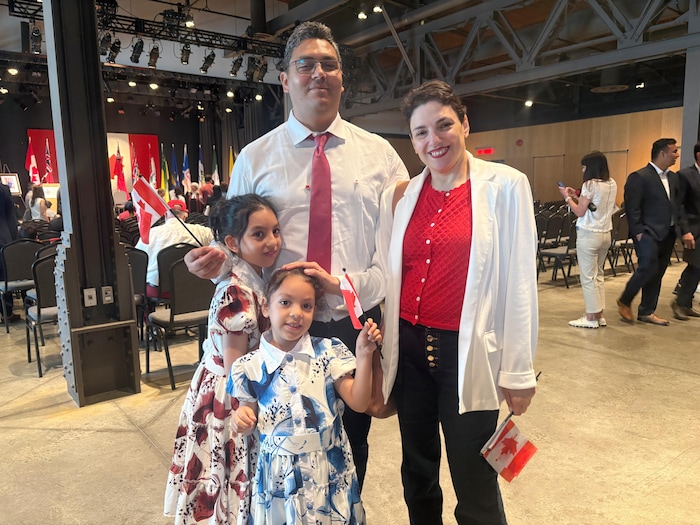Un homme portant chemise blanche et cravate rouge, une femme portant blouse rouge et veston blanc, une petite fille en robe rouge et sa sœur en robe bleue posent ensemble avec de petits drapeaux du Canada.