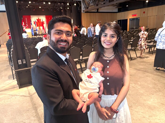 Un jeune couple souriant. Le père tient dans ses bras un bébé vêtu d'un pyjama d'une pièce blanc avec une feuille d'érable rouge.