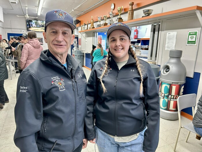 Un homme et une femme côte à côte dans l'aréna, portant des manteaux avec le logo des pompiers locaux.