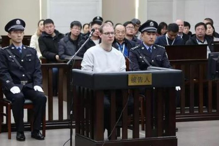 Un homme est assis dans le box des accusés flanqué de deux policiers chinois.