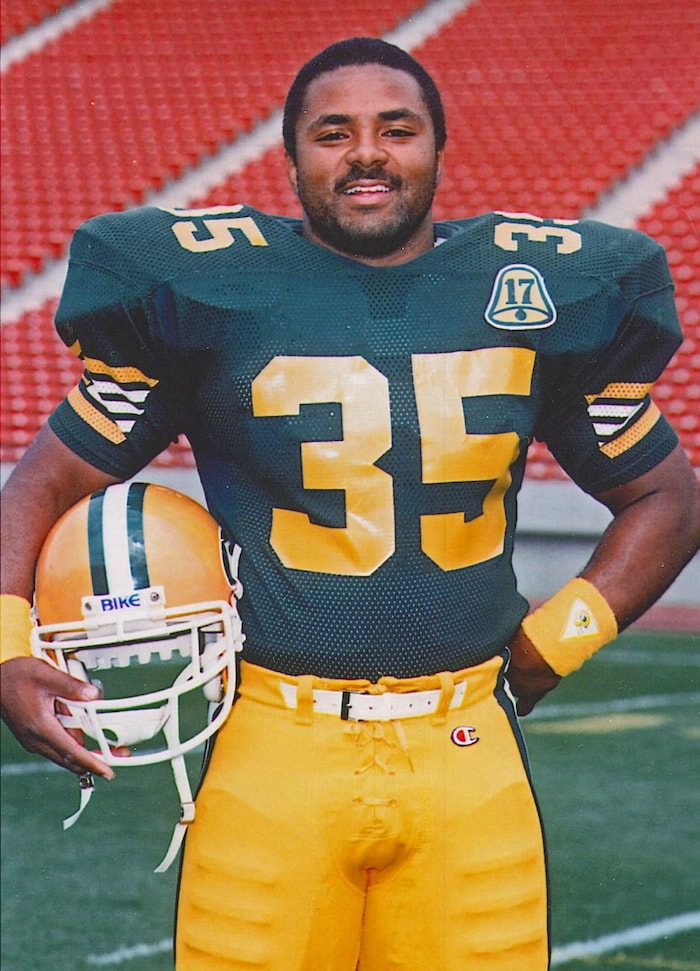 Un joueur de football en uniforme vert et jaune pose pour une photo, son casque sous le bras, sur le terrain.