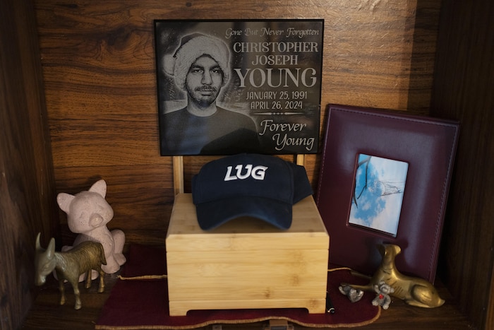 Une petite boîte en bois, avec un portrait en noir et blanc d'un jeune homme, entourée de quelques objets, dont une casquette.