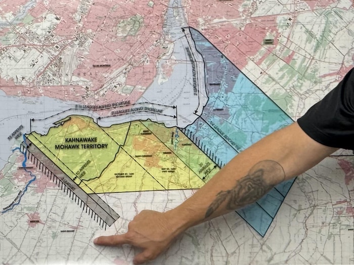 Une main désigne les contours colorés d’un territoire sur une grande carte géographique.