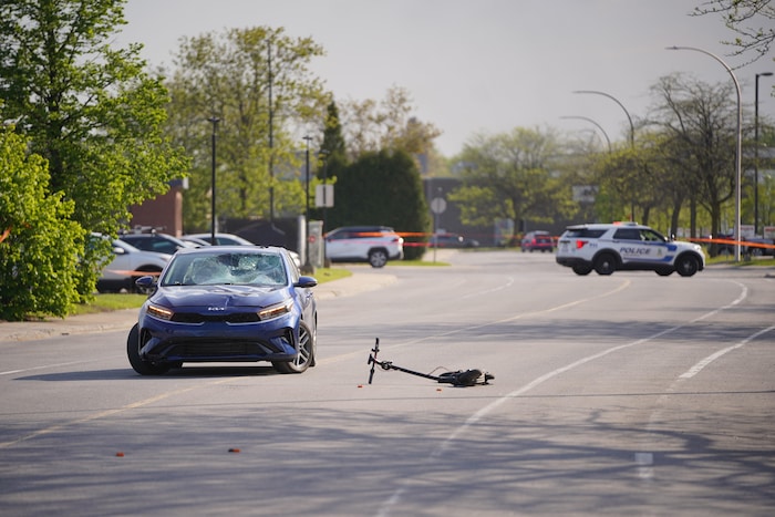 Une trottinette par terre à côté d'une voiture accidentée.