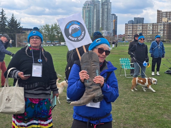 Une femme vêtue d'une tuque bleue et d'un blouson bleu brandit une botte de cowboy en cuir marron surmontée d'une pancarte affichant le slogan « Water Not Coal » (De l'eau, pas du charbon) lors d'un rassemblement.