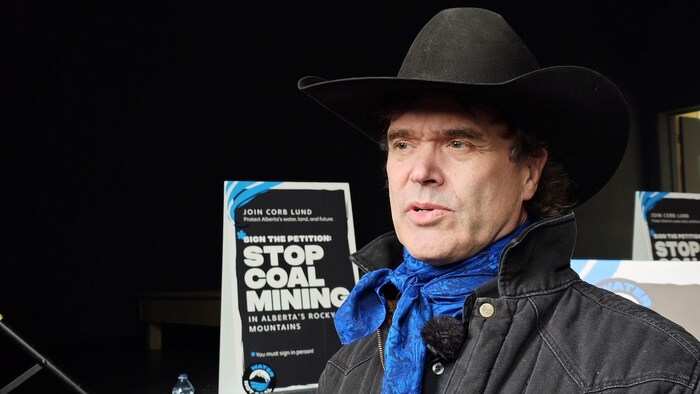 Le chanteur albertain Corb Lund donne une entrevue. Il se tient devant des affiches prônant la fin de l'exploitation minière du charbon.