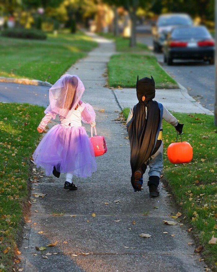 Deux enfants courent dans la rue avec des sacs pour ramasser des friandises. Ils sont déguisés pour l'Halloween.