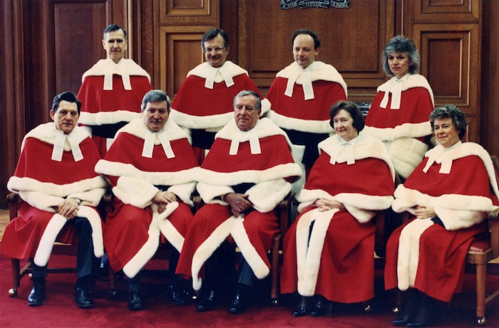 Neuf juges en longue toge rouge et blanche posent pour une photo à la Cour suprême. Cinq sont assis à l'avant et les quatre autres sont debout derrière eux.