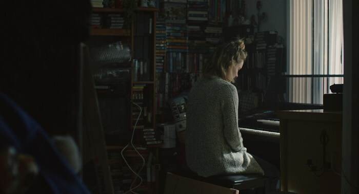 Une femme devant une mur de disques. Elle est assise devant un clavier pour jouer de la musique.