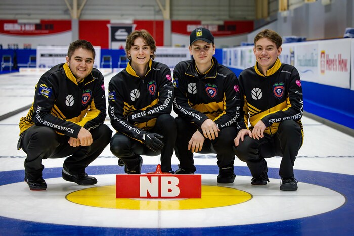 Photo de groupe des quatre membres de l'équipe masculine de curling du Nouveau-Brunswick, en uniforme noir et jaune. Ils sont agenouillés sur la glace devant une pierre de curling.