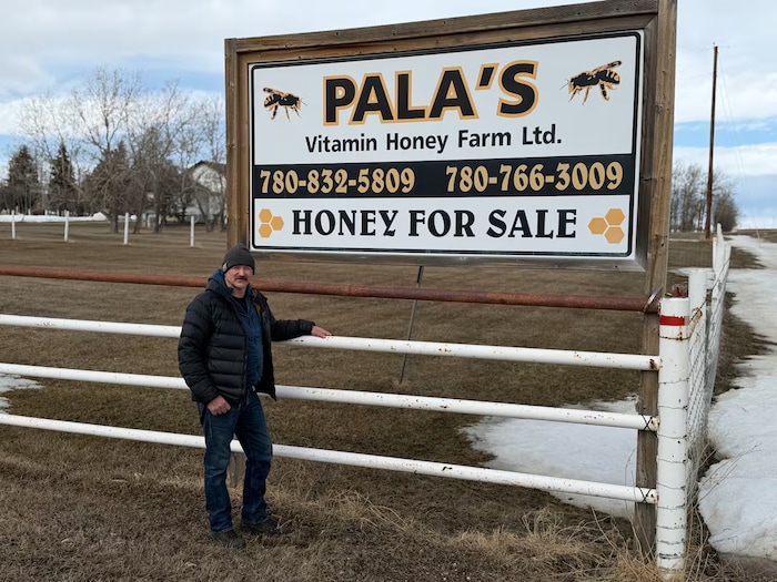 Un homme se tient devant un panneau indiquant sa ferme apicole, dans le nord de l'Alberta, avril 2026.