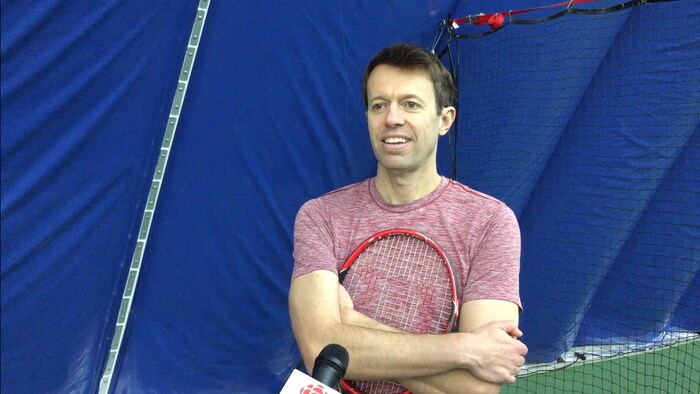 Un homme qui porte un t-shirt rouge et qui tient une raquette de tennis