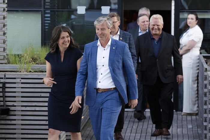 Tim Houston et Danielle Smith marchent côte à côte en souriant sur une passerelle en bois, pendant que les autres premiers ministres, derrière eux, s'engagent sur le même chemin.