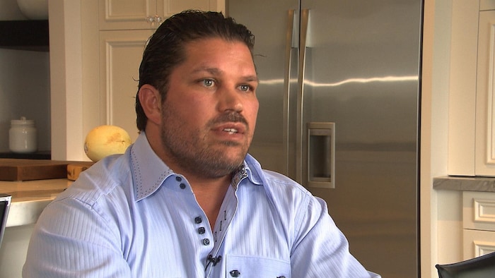 Dannick Lessard est assis dans sa cuisine, devant son réfrigérateur