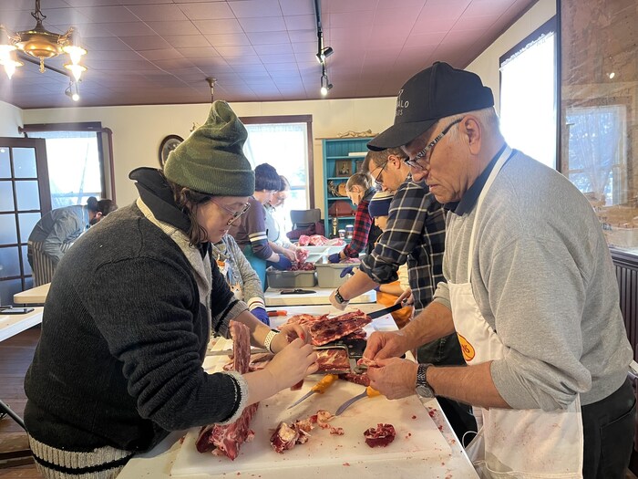 Des personnes dans une pièce manipulent de la viande sur une table le 13 décembre 2025 à Saint-Pierre-Jolys.