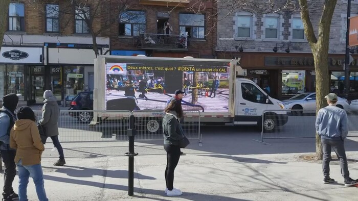Un camion devant un commerce qui montre aux gens en file sur le trottoir la distance qu'ils maintiennent entre eux.