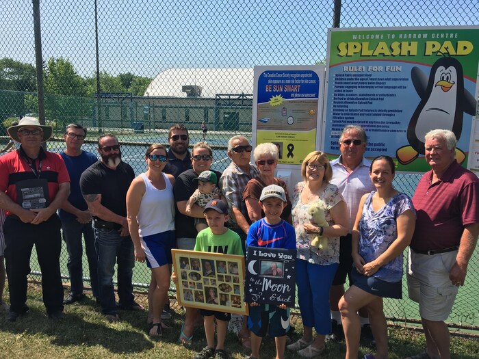 Une famille d'environ une douzaine de personnes avec des gens de tous les âges posent pour la caméra devant le distributeur de crème solaire.