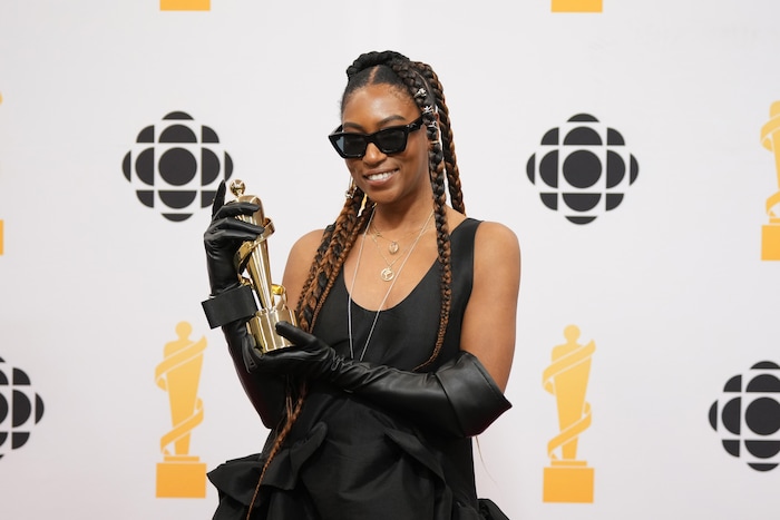 A woman in a black dress and sunglasses poses with a trophy.